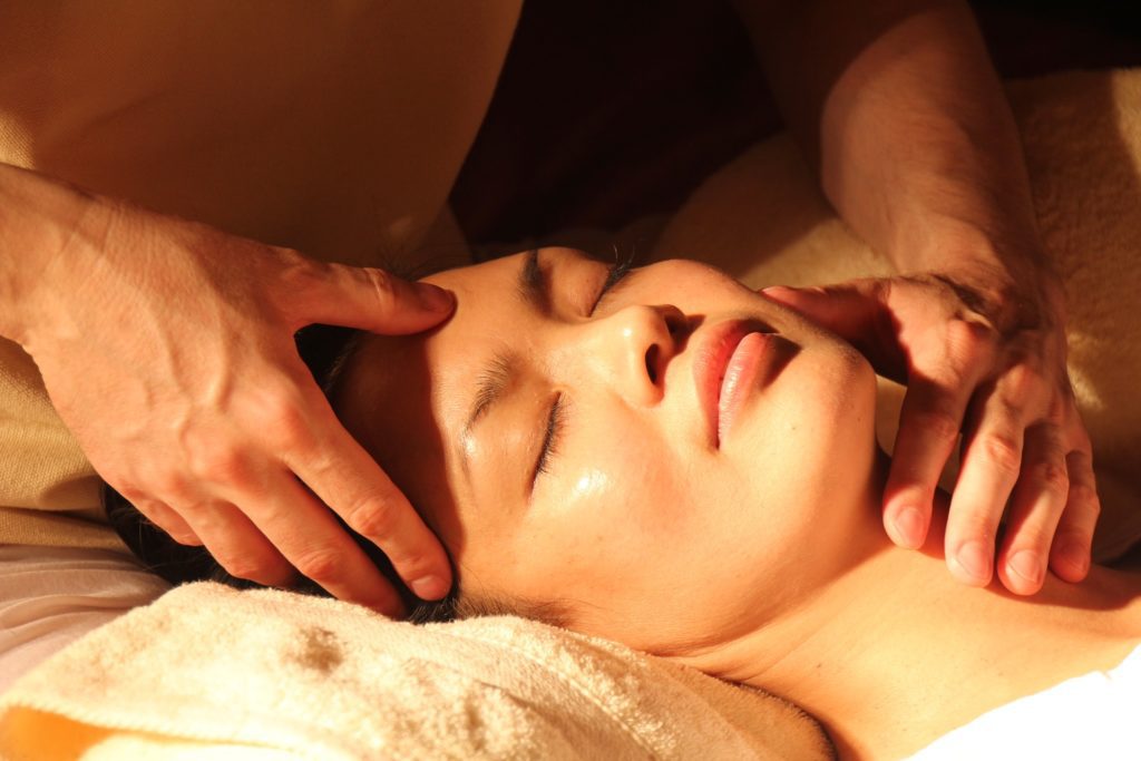 Une personne utilise les points marmas pour faire un massage et détendre la tête d'une femme allongée et reposée sur un coussin