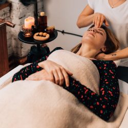 Une personne masse la tête d'une femme allongée et détendue sur une table selon le massage métamorphique